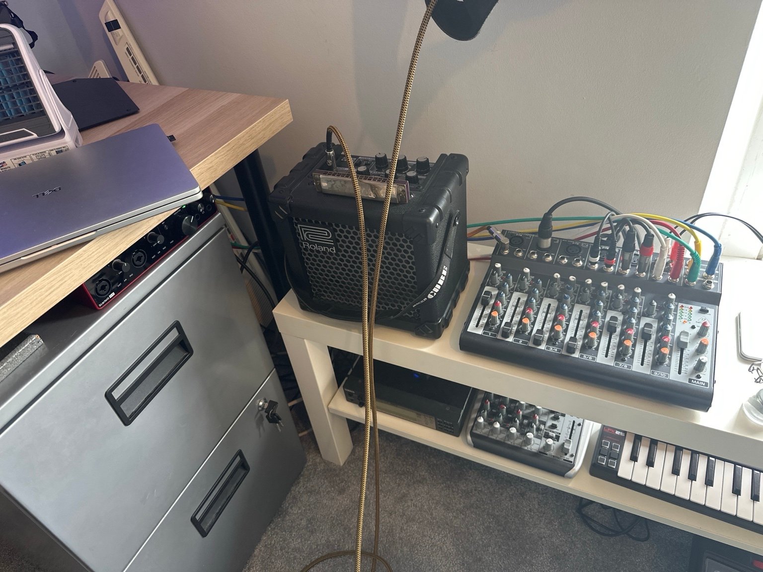 Corner of Tim’s home studio with a Focusrite Scarlett interface, Roland Cube amplifier, mixer, small keyboard and cabling arranged beside the desk.